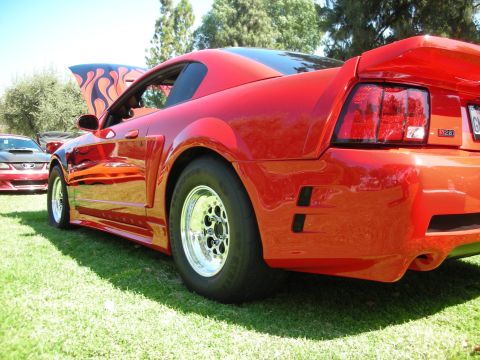 1998 Ford Crown Victoria - A red Ford Mustang with racing slicks and flame decals on the hood is displayed at a car show, with another Mustang visible in the backgrou…