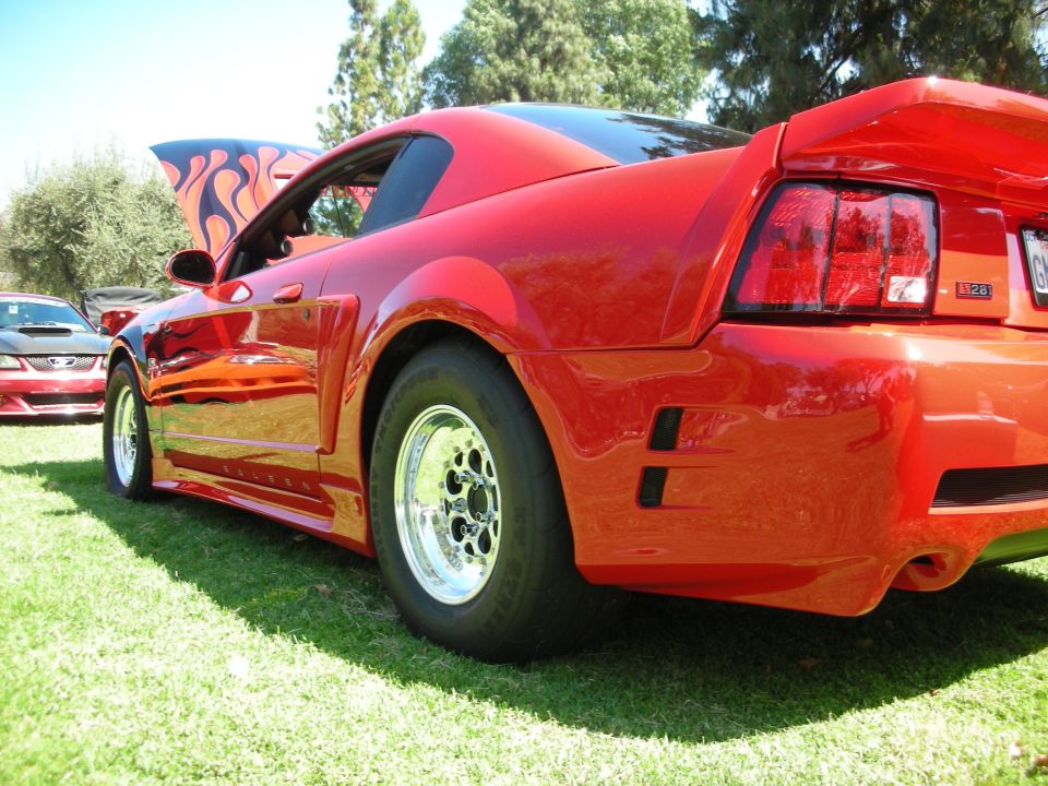Red Ford Mustang rear quarter view with racing slicks and flame decals on hood