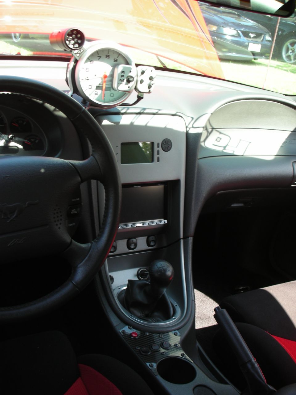 Interior view of a car, showing a steering wheel, dashboard with gauges, and a manual shifter. Another car is visible through the windshield