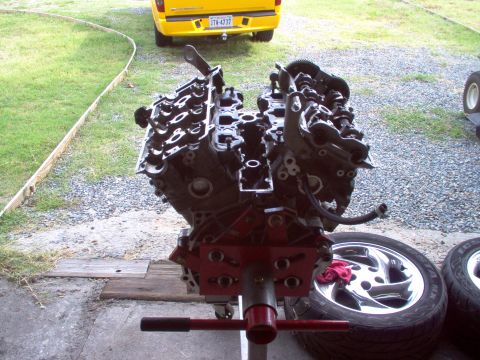 1996 Ford Probe - Engine assembly on a stand with chrome wheels and a yellow truck in the background.