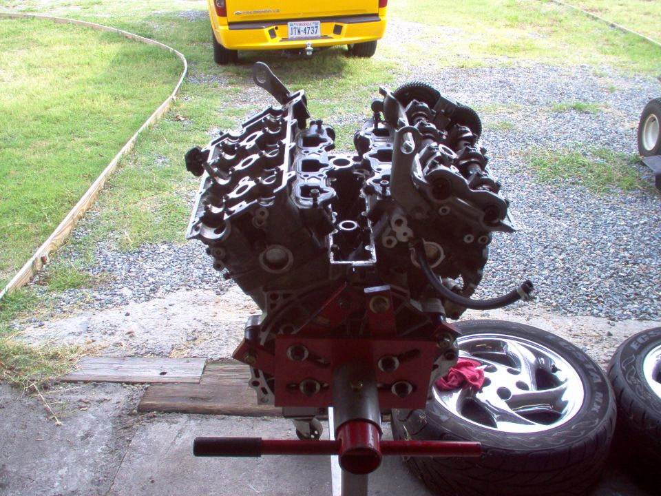 Engine on red stand, chrome wheels nearby, yellow truck in background