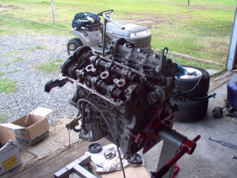 1996 Ford Probe - Engine on a stand with parts scattered around, lawn tractor visible in background.