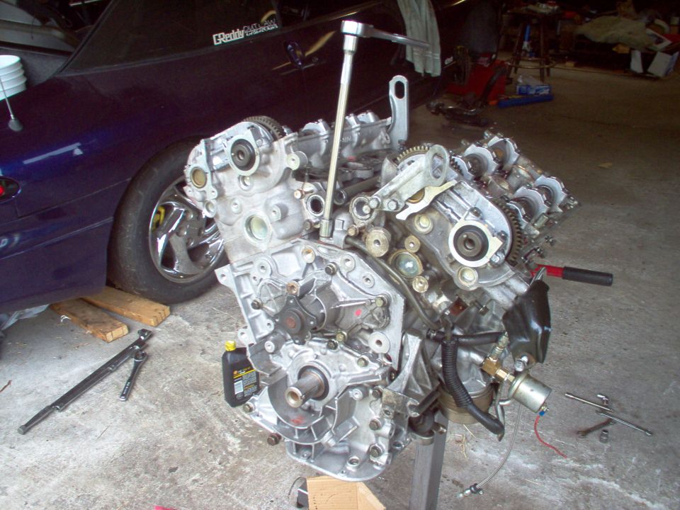 Engine on a stand in a garage, with a dark blue car in the background