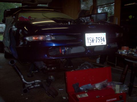 1996 Ford Probe - The front of a blue coupe is shown with its hood up, indicating it is in a garage for repairs or modifications.