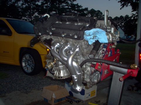 1996 Ford Probe - Engine removed from a vehicle and placed on a stand, with a yellow truck nearby.