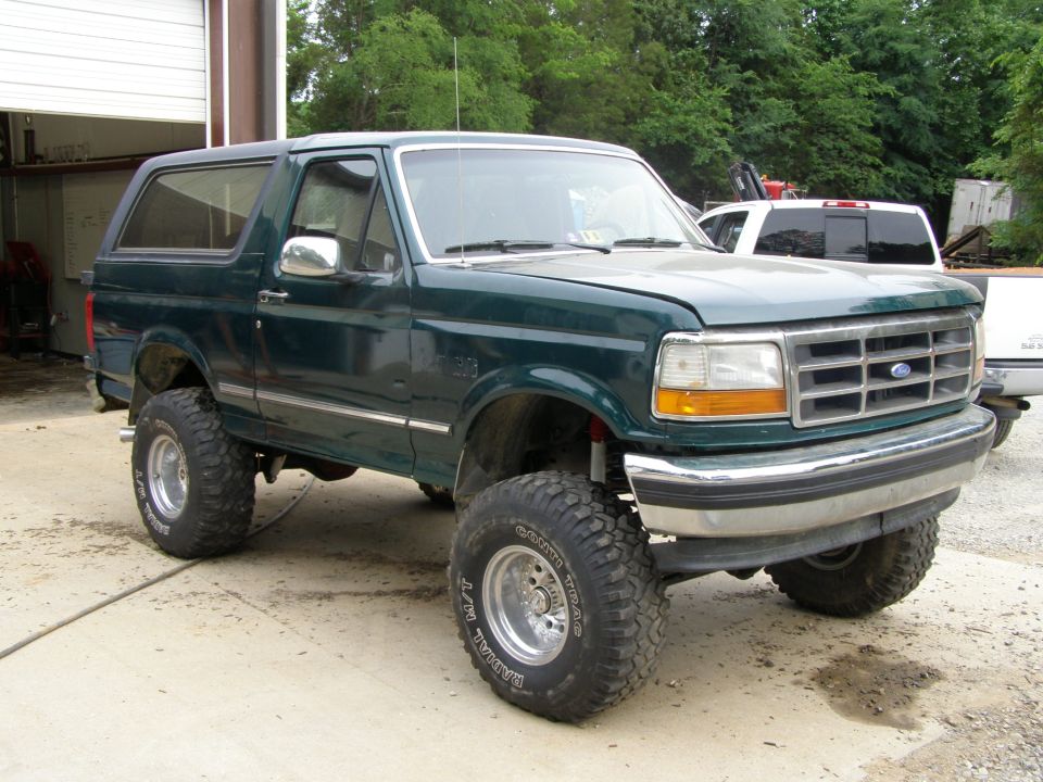 Green Ford Bronco with lifted suspension and off-road tires parked outside a garage