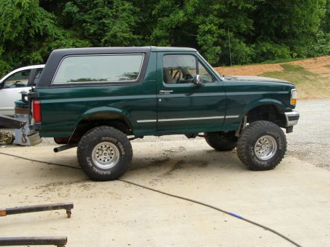 1993 Ford Bronco - This lifted Ford Bronco is shown from the side, a dark green body and a black removable top.