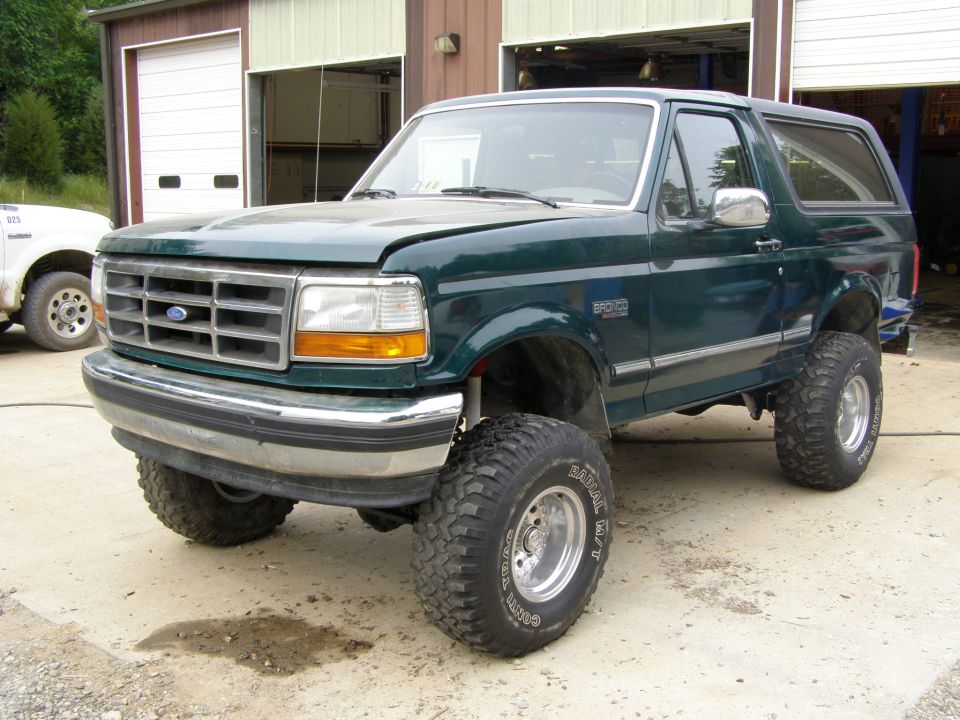 Green Ford Bronco with lifted suspension and large tires parked in front of a garage