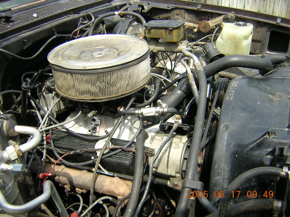 Dirty carbureted V8 truck engine bay with round air cleaner and tangled wiring