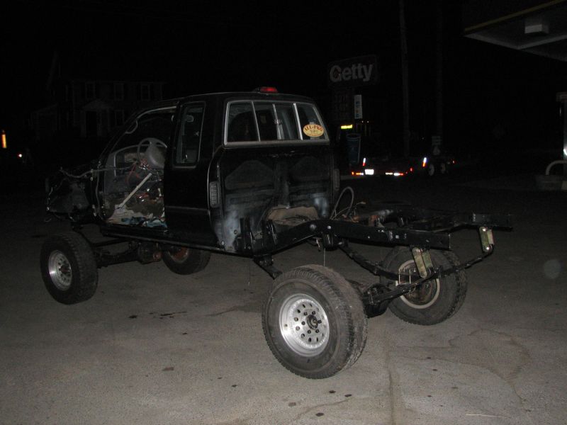 black truck body on a bare chassis, doors open, engine bay exposed, at night