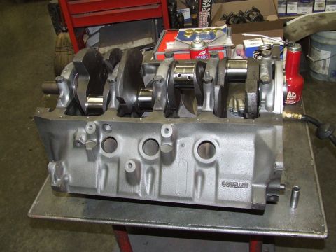1979 Ford Bronco - An engine block with a crankshaft installed sits on a workbench, surrounded by automotive parts and tools.
