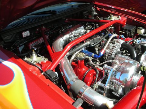 1998 Ford Crown Victoria - Customized engine bay a polished supercharger and vibrant red structural supports, with flame graphics visible on the fender.