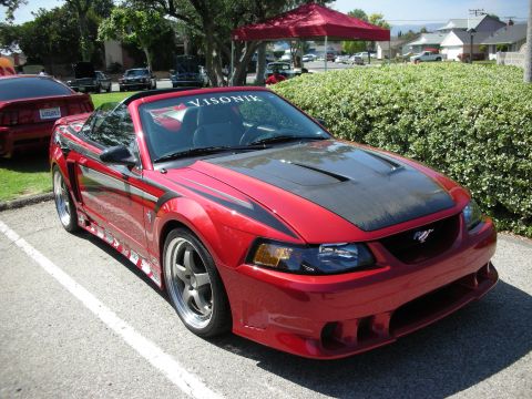 1998 Ford Crown Victoria - Red convertible Mustang with carbon fiber hood and racing stripes, parked next to another red Mustang.
