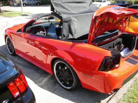 1998 Ford Crown Victoria - Red convertible Mustang with trunk open, revealing subwoofers. Another Mustang is partially visible in the foreground.