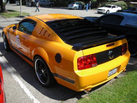 1998 Ford Crown Victoria - A yellow Ford Mustang with racing stripes and louvers is parked in a lot next to other vehicles.