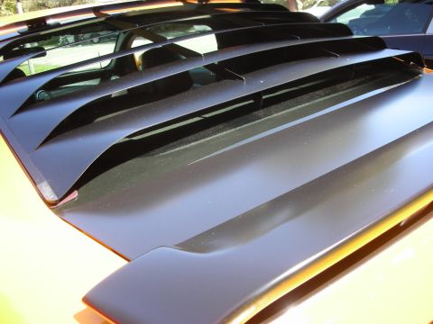 1998 Ford Crown Victoria - A close-up view of a black hood scoop with louvers on an orange vehicle.