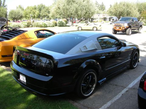 1998 Ford Crown Victoria - A black Ford Mustang is parked at an outdoor car show, with a yellow Mustang visible to its left.