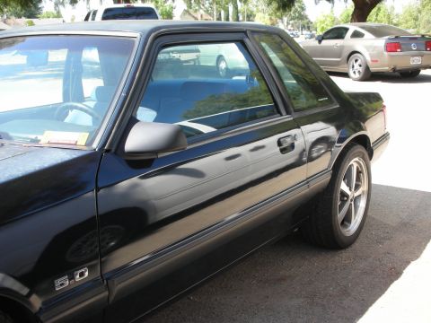 1998 Ford Crown Victoria - Side view of a black Ford Mustang, showing the 5.0 badge and a second vehicle in the background.
