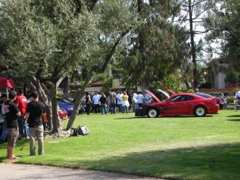 1998 Ford Crown Victoria - A red Ford Mustang with custom flame decals is displayed with its hood open at an outdoor car show.