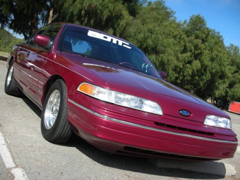 1998 Ford Crown Victoria - A maroon 1998 Ford Crown Victoria is parked outdoors, angled towards the camera with a banner across its windshield.