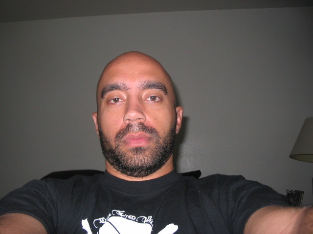 Bald man with beard wearing a black t-shirt, looking at the camera