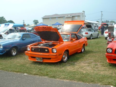 1978 Ford Mustang II - An orange 1978 Ford Mustang II is displayed with its hood and trunk open at an outdoor car show.