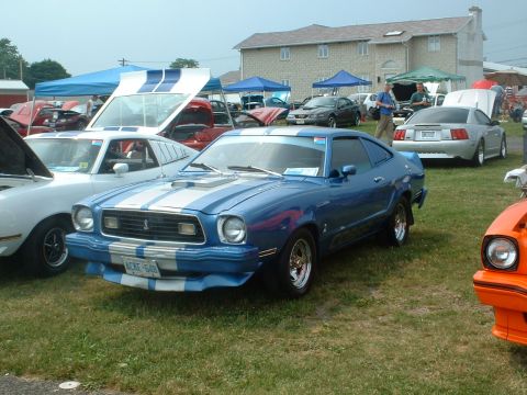 1978 Ford Mustang II - Blue 1978 Ford Mustang II with racing stripes at an outdoor car show.