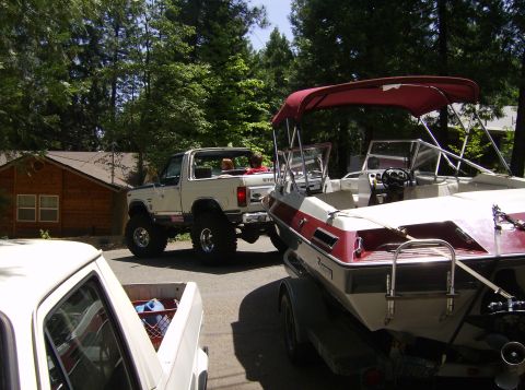 1986 Ford Bronco - A lifted SUV is parked next to a boat on a trailer.