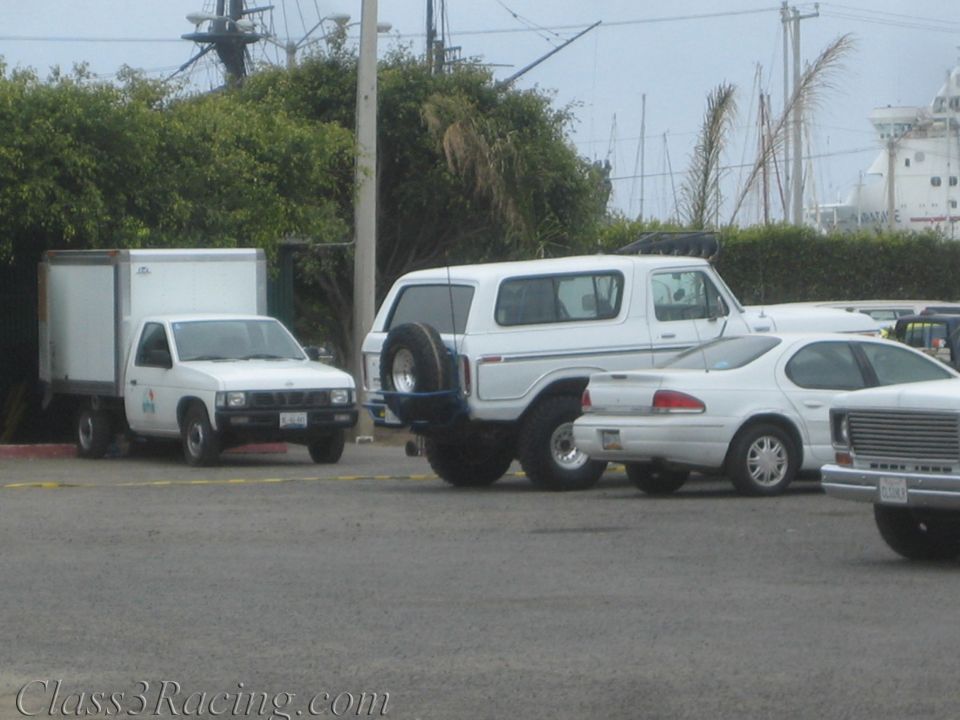 White Ford Bronco with spare tire parked in lot near harbor among other vehicles