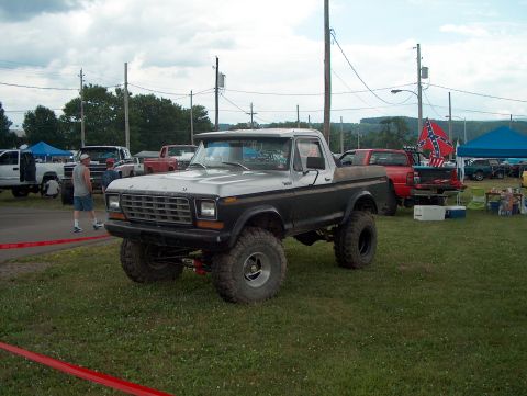1978 Ford Bronco - A lifted pickup truck is parked on grass with other vehicles in the background under a cloudy sky.