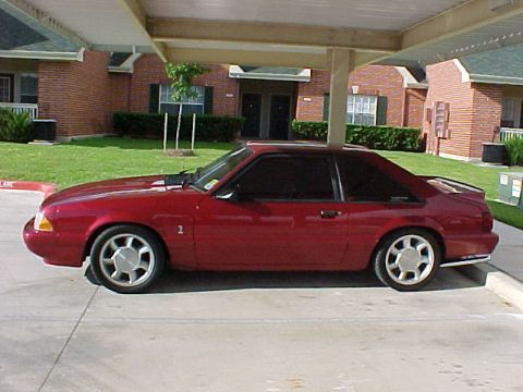 1992 Ford Mustang - A red coupe with distinctive wheels is parked under a covered area.