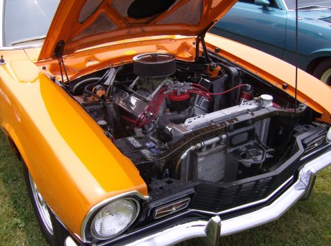 1970 Ford Ranchero - The engine bay of an orange 1970 Ford Ranchero is visible, with another vehicle in the background.