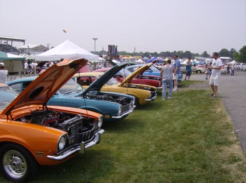 1970 Ford Ranchero - A line of classic cars, including an orange 1970 Ford Ranchero, are displayed at an outdoor event.