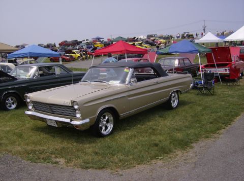 1970 Ford Ranchero - A classic convertible is displayed at a car show with many other vehicles and tents visible.