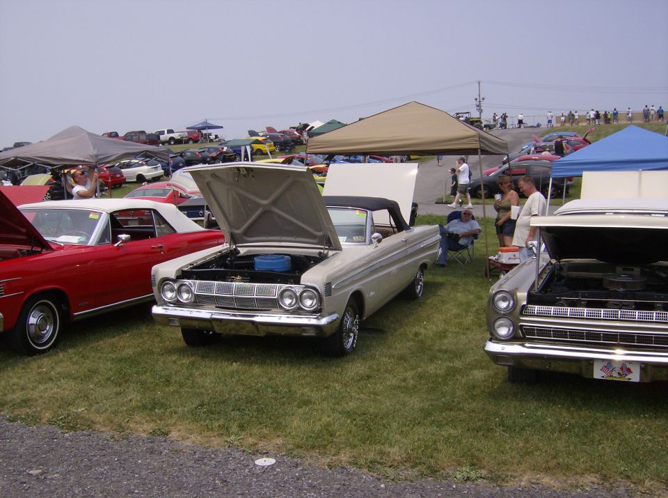 Beige 1964 Ford Falcon convertible with hood open, parked on grass at a car show