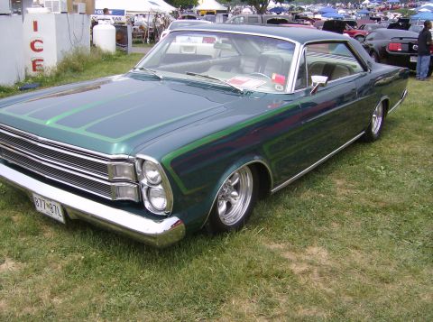 1970 Ford Ranchero - A green coupe with custom racing stripes sits on a grassy field at an outdoor event.