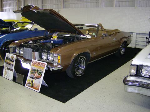 1970 Ford Ranchero - A brown 1973 Ford Cougar convertible is displayed with its hood open, next to other vehicles.