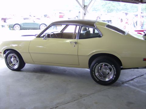 1970 Ford Ranchero - A yellow Ford Maverick coupe with a brown vinyl top is parked indoors, with other vehicles in the background.
