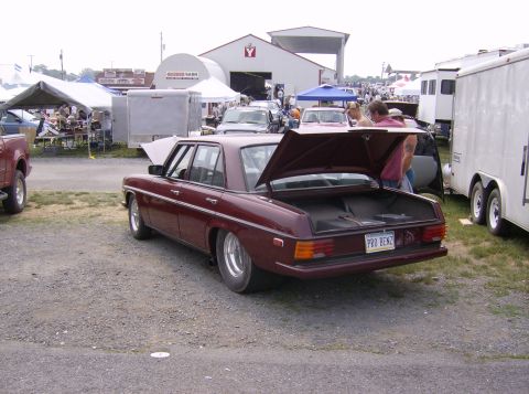 1970 Ford Ranchero - A maroon sedan with its trunk open is parked at an outdoor event, with other vehicles and tents visible in the background.