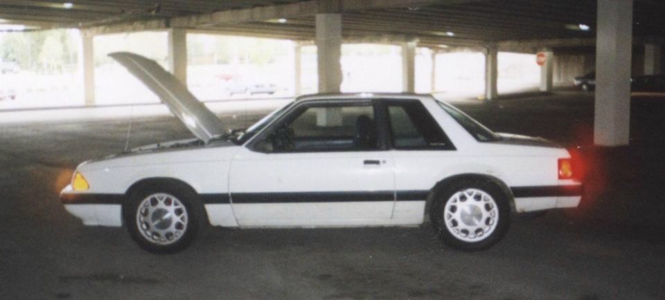 White 1992 Ford Mustang coupe with hood open, parked under a concrete structure