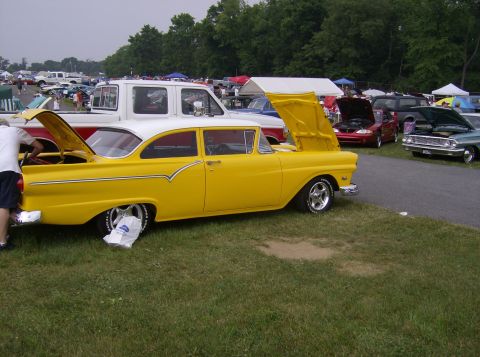 1970 Ford Ranchero - A yellow 1955 Ford Fairlane sedan is displayed with its hood and trunk open at an outdoor event.