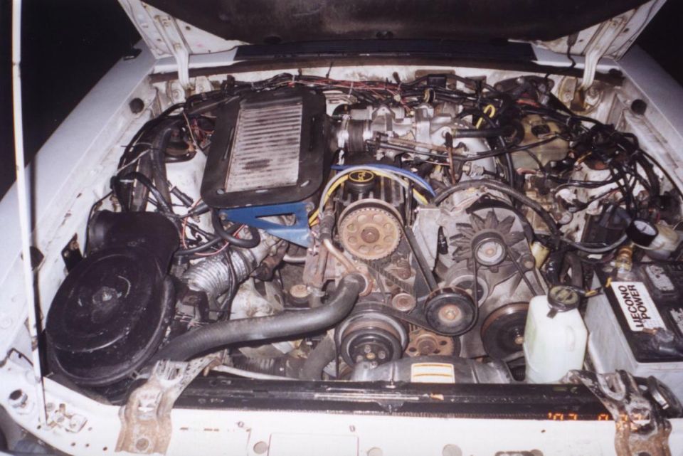 Engine bay with hoses, belts, and engine components visible. A battery labeled 'LIEGONO POWER' is on the right