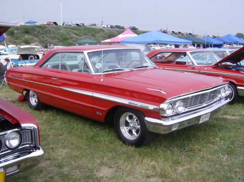 1970 Ford Ranchero - A bright red 1964 Ford Galaxie 500 coupe is parked on grass at an outdoor car show, with other vehicles and tents in the background.