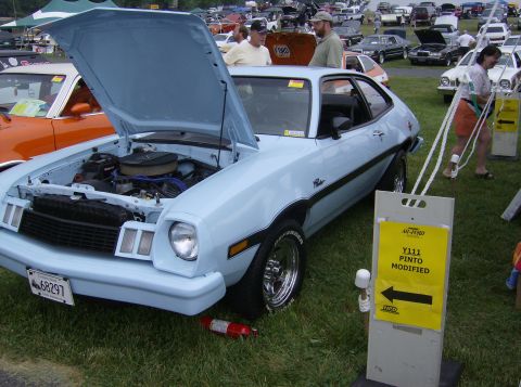 1970 Ford Ranchero - A light blue Ford Pinto is displayed with its hood open at an outdoor car show, with other vehicles visible in the background.