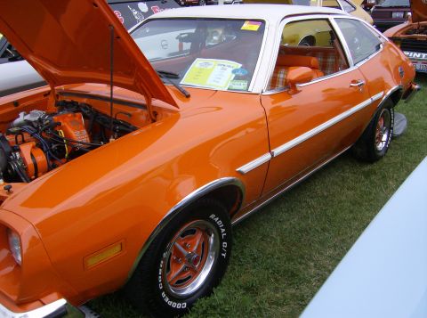 1970 Ford Ranchero - This orange coupe, likely from the 1970s, has a white roof and a plaid interior.