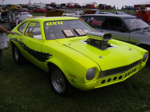 1970 Ford Ranchero - A bright lime green drag car with a large blower scoop and black graphics is parked on grass, with other vehicles in the background.