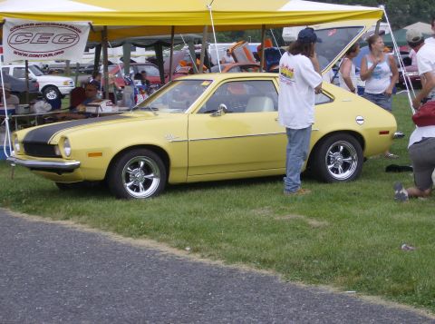 1970 Ford Ranchero - A yellow Ford Pinto coupe is parked on grass with people around it.