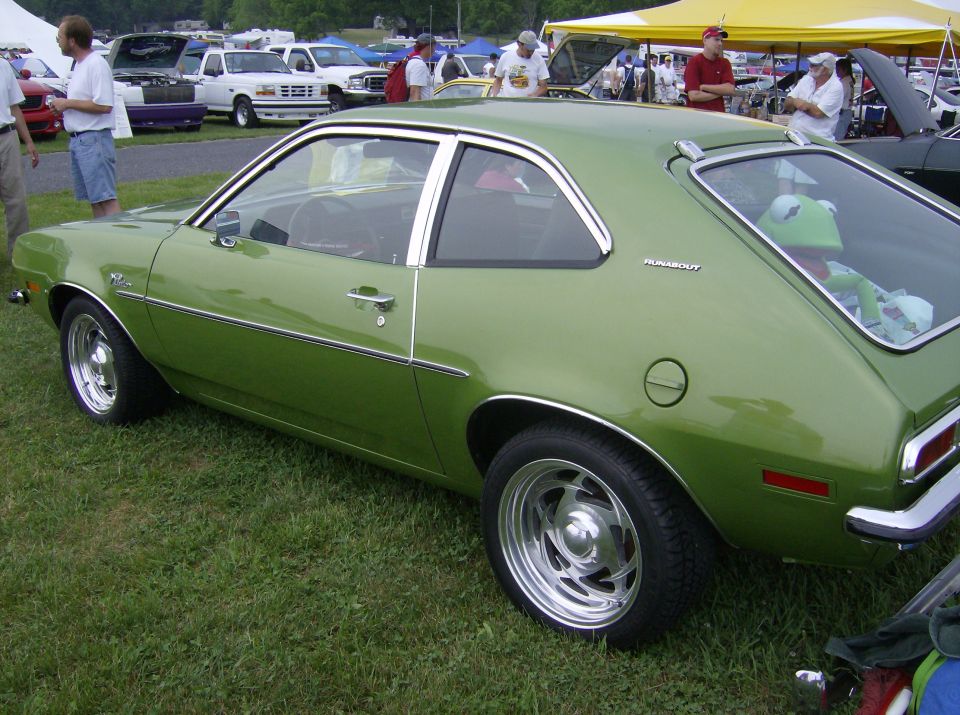 Green 1975 Ford Pinto coupe with chrome wheels and a Kermit the Frog doll in the rear window