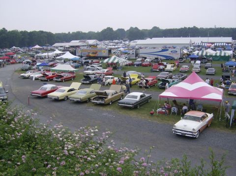 1970 Ford Ranchero - A wide view of a car show numerous classic vehicles parked in rows under a cloudy sky.