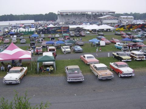 1970 Ford Ranchero - A large gathering of classic cars at an outdoor event, with tents and grandstands visible.